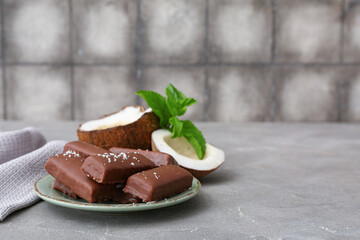 Plate with tasty chocolate covered coconut candies on table