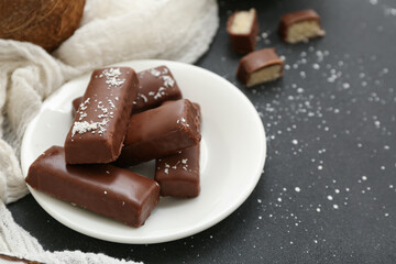 Plate with tasty chocolate covered coconut candies on black background