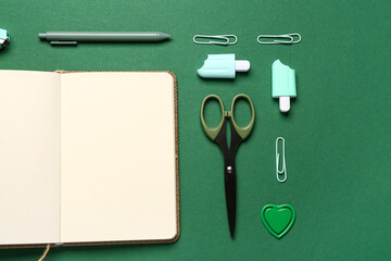 Notebook with different stationery supplies on green background