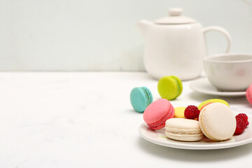 Plate with sweet macaroons and raspberries on white background