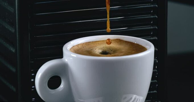 Super slow motion macro of hot creamy aromatic espresso coffee is poured in white porcelain mug from coffee machine for being served to customer at cafe or bar at 1000 fps.