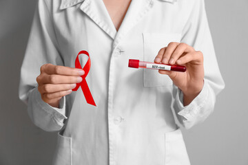 Doctor holding HIV blood test tube and red ribbon on grey background