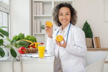 Mature female nutritionist with orange at table in office