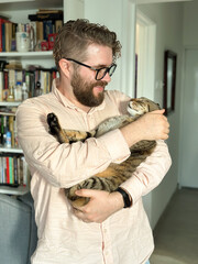 Handsome millennial man holds a tabby cat in his arms and kisses it. Pet and friendship concept