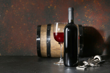 Wooden barrel, opener, bottle and glass of red wine on black table against grunge brown background
