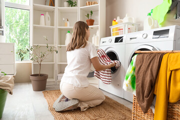 Young woman putting stained t-shirt into washing machines in laundry room