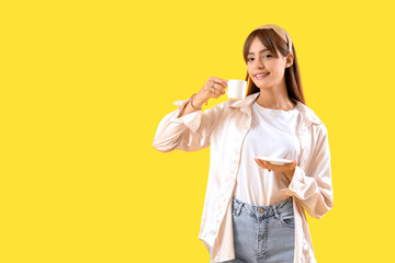 Beautiful young woman with cup of coffee on yellow background