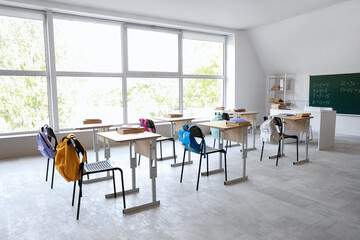 Interior of empty classroom with desks, backpacks on chairs and blackboard