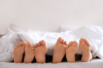 Feet of young man with two women lying under blanket in bedroom, closeup. Polyamory concept