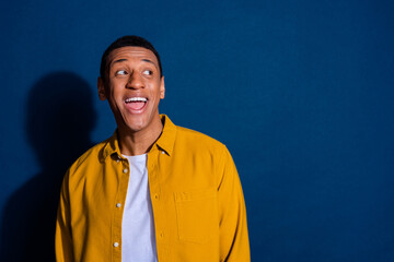 Photo of surprised guy wearing yellow shirt laughing looking empty space nice proposition isolated on dark blue color background