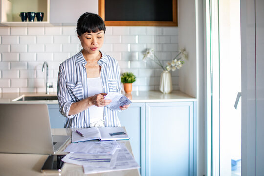 Focused woman organizing bills and paperwork in kitchen
