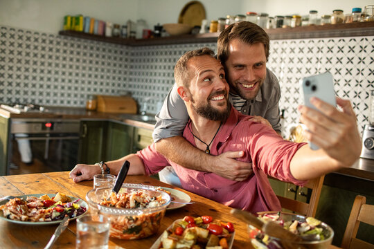 Gay couple enjoying lunch together at home and taking selfie