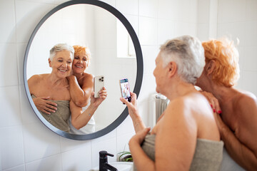 Senior lesbian couple examining their skin in the mirror after shower