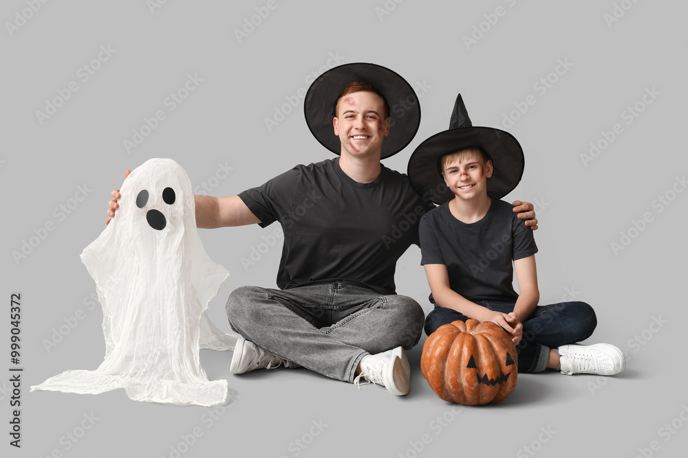 Wall mural Father with his son dressed for Halloween as wizards and decor sitting on light background