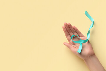 Female hand with light blue ribbon on yellow background. World Cancer Day