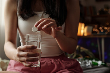 Hands of unrecognizable teenage girl putting effervescent pill into glass of water while suffering from hangover in the morning