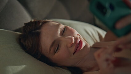 Girl smartphone lying bed pillows waking up early morning close up. Sleepy woman