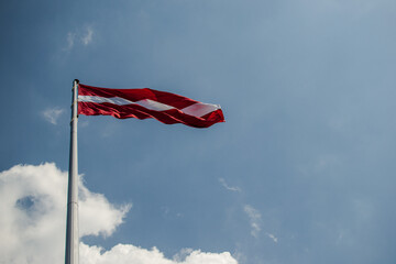 Latvian flag on flagpole against blue sky