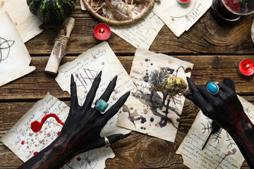 Bloody black witch hands with magic attributes and dry flowers on brown wooden background....