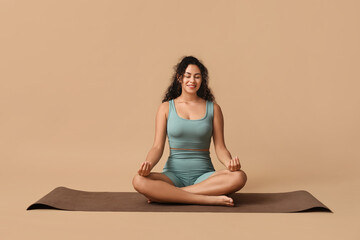 Sporty young African-American woman practicing yoga on mat against brown background