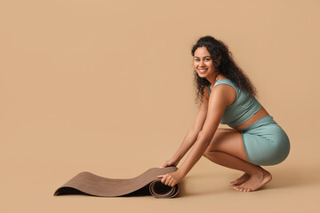 Sporty young African-American woman with yoga mat on brown background