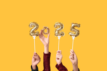 Female hands with figure 2025 made of foil balloons and Christmas decoration on yellow background