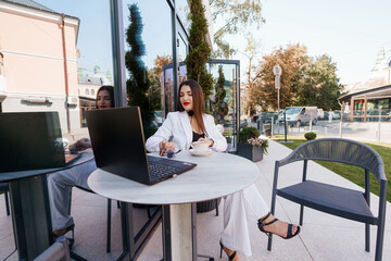 Elegant Business Woman in a Chic Outdoor Cafe Setting with Laptop and Coffee