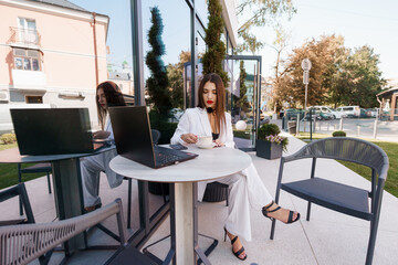 Elegant Businesswoman Enjoying Coffee Outdoors While Working on Laptop in Stylish Urban Setting