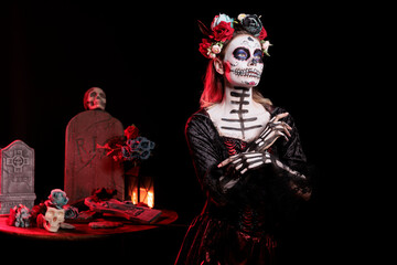 Fototapeta premium Woman with flower wreath on head at Day of the Dead event to remember the deceased, celebrating their memory. Lady wearing gothic corpse makeup for holiday of remembrance for those who have passed