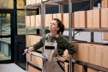 Delivery service employee searching clients parcel in warehouse checking clipboard with online...