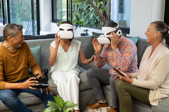 Using VR headsets, senior diverse friends enjoying virtual reality experience together, at home - Powered by Adobe