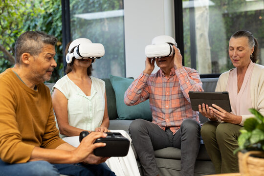 Using VR headsets, senior diverse friends enjoying virtual reality experience together, at home - Powered by Adobe