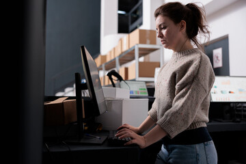 Warehouse manager standing at counter desk, analyzing merchandise logistics on computer. Stockroom worker checking customers online orders preparing packages for shipping in storehouse