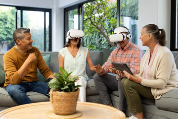 Enjoying virtual reality, senior diverse friends using VR headsets together indoors, at home