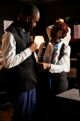 Seamstress helping african american client try on bespoken sartorial piece after finishing needlework comission. Customer happy with fitting elegant attire made in minority owned atelier shop