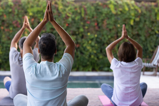 Practicing yoga outdoors, senior diverse friends meditating on yoga mats by pool, at home