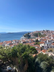 Fototapeta premium Panoramic View of Skiathos Town Greece – Scenic coastal hillside with white buildings and terracotta rooftops overlooking the Aegean Sea under clear blue skies