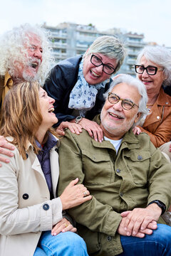 Vertical. Group of seniors grey hair joyful people having fun together sitting on bench in urban. Cheerful mature Caucasian friends meeting talking funny enjoying free time laughing autumn day outdoor