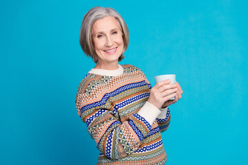 Photo of good mood retired woman with white gray hair wear ornament sweater hold cup of cappuccino isolated on blue color background