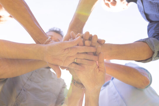 Senior diverse friends stacking hands together, showing unity and teamwork outdoors, at home