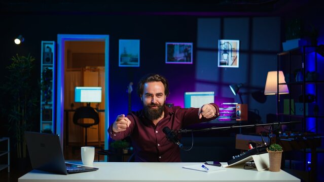 Playful online star using tech equipment to shoot video, doing frantic gesturing. Energetic content creator jumping on chair, having fun while filming vlog with professional mic in studio, camera B