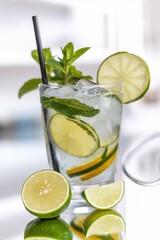 Fototapeta premium Refreshing summer cocktail with lime, mint, and ice in a clear glass with a black straw.