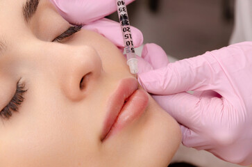 Young woman gets filler injection in her lips at a beauty salon. Lip augmentation procedure.