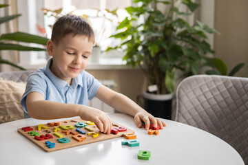 A Caucasian light-haired boy of five years old with blue eyes is putting together a puzzle