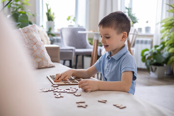 A Caucasian light-haired boy of five years old with blue eyes is putting together a puzzle