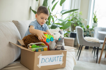 Boy child puts toys in a cardboard box for charity. Donation concept.