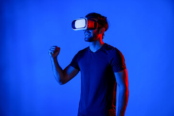 Professional gamer using VR goggle while cheering game competition. Happy man wearing casual cloth and virtual headset while watching at football competition at neon background. Innovation. Deviation.