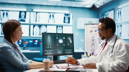 Medical expert discussing about diagnostics treatment with patient in cabinet, reviewing the test analysis reports during a consultation. Medic specialist supporting woman with illness. Camera B.