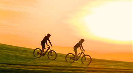 Obraz premium AERIAL: Golden evening sunbeams shine on mountain bikers speeding down a grassy hill in the beautiful Slovenian mountains. Scenic drone view of active people riding e-bikes in the scenic Dolomites.