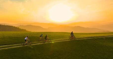 AERIAL: Golden sunbeams shine on a bike trip expedition riding in the picturesque mountains of Slovenia. Flying along five friends mountain biking in the verdant Alps at beautiful autumn sunset.